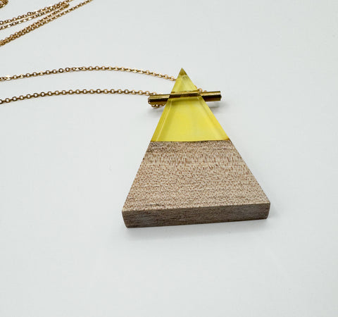 A wooden triangle-shaped pendant with a gold-colored metal chain and a resin tube necklace.