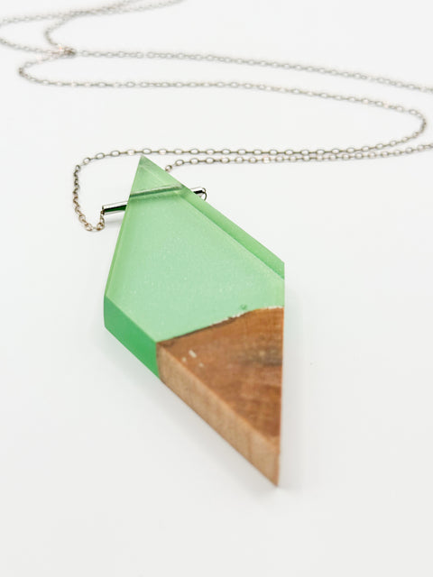 Rhombus wood and a green resin pendant in a silver chain necklace in a white background.