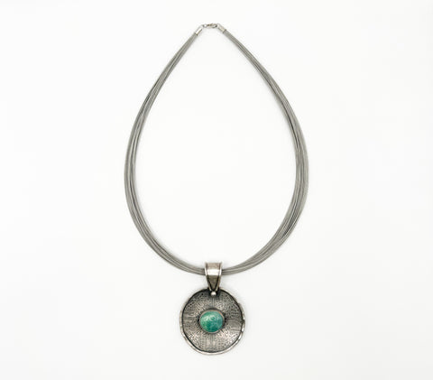 A silver necklace holding a pendant with a light blue stone.