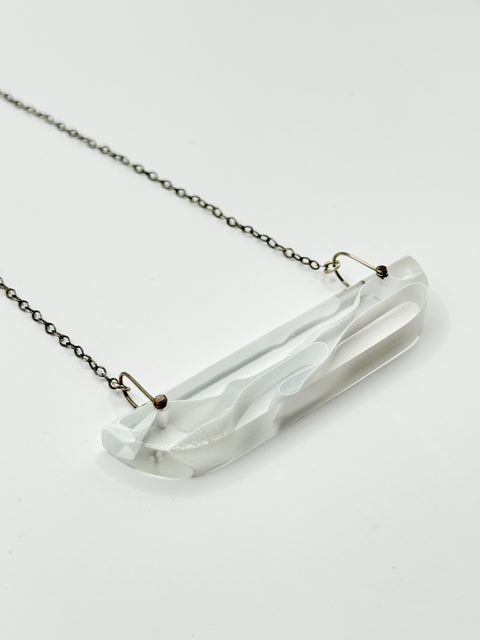 A thin white/clear resin wave-shaped pendant necklace with a metallic chain.