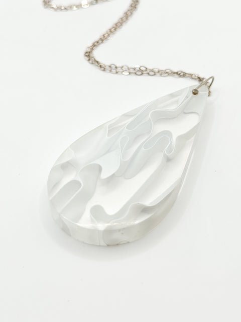 A silver-colored necklace with a teardrop-shaped resin pendant featuring a wave-like pattern, attached to a chain.