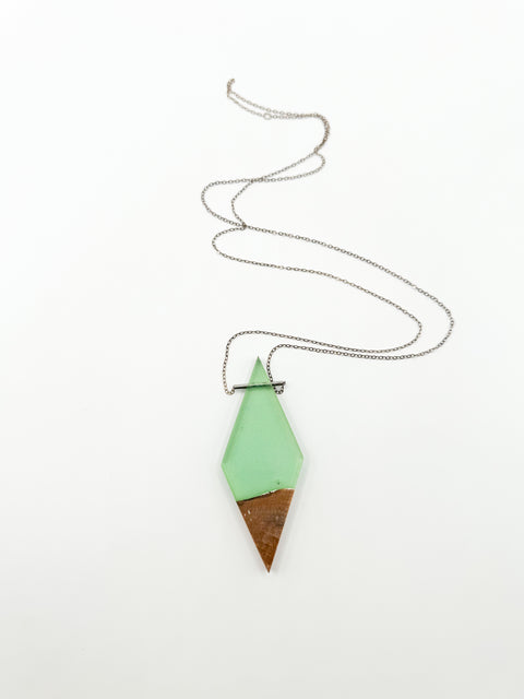 Rhombus wood and a green resin pendant in a silver chain necklace in a white background.