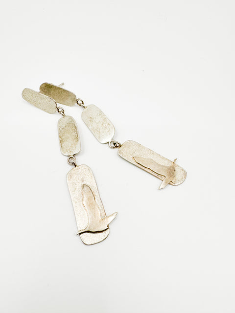A pair of silver earrings designed to resemble a bird in flight, with tiered cut-out patterns.