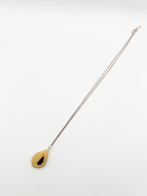 A gold-colored feather-shaped shadowbox pendant with a visible insect silhouette, attached to a silver chain.