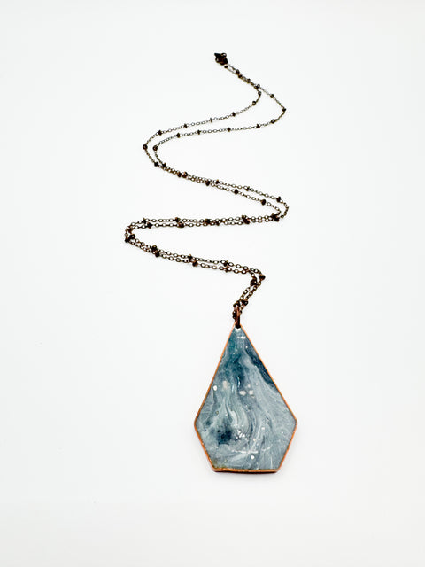 A marbled trapezoid-shaped necklace with a metallic chain and a teardrop-shaped pendant.