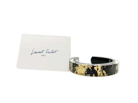 A two-tone (gold and black) bangle bracelet next to a business card with the name 'Laurent Guillot' written on it.