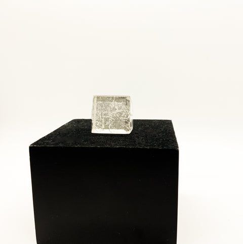 A silver ring with a faceted design, displayed on a black square-shaped box.