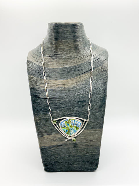 A sterling silver necklace with a geometric enamel pendant featuring blue and green colors, displayed on a textured grey mannequin.