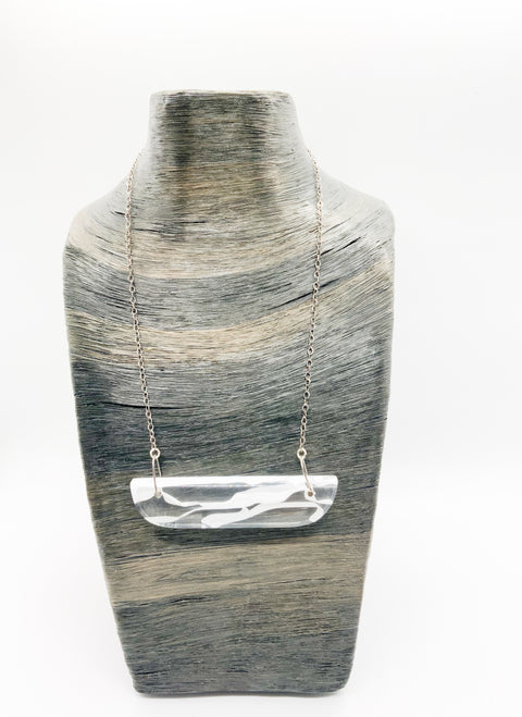A thin white/clear resin wave-shaped pendant necklace with a metallic chain displayed on mannequin.