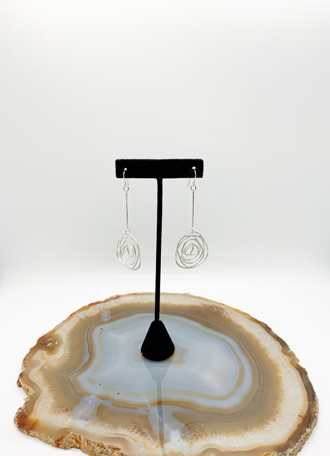 Earrings on a black stand with a natural stone base on a white background