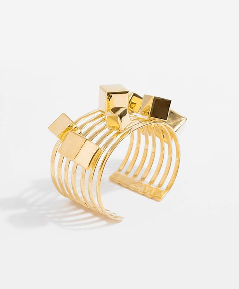 A gold cube bangle bracelet with a cuff design, featuring various sizes of gold cubes on an adjustable band.