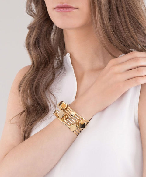 A model wearing a gold cube bangle bracelet with a cuff design.