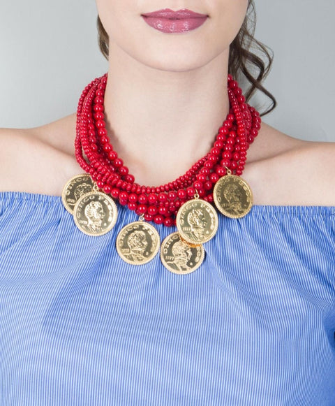 A person wearing a blue off-shoulder top and a multi-layer red bead necklace with gold-colored coins.