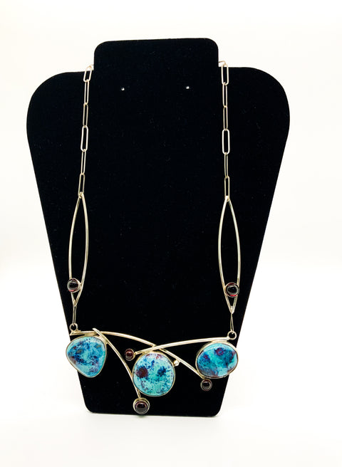 A sterling silver necklace with blue pottery stones and red garnets displayed on a black mannequin.