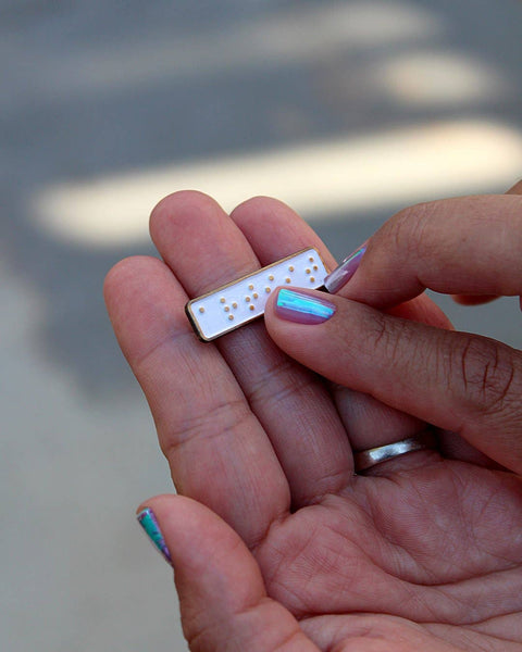 Small rectangular pin with raised dots held between fingers against a blurred background