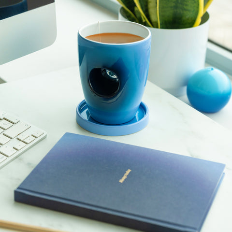 Blue mug with a black object inside on a desk with a notebook and keyboard.
