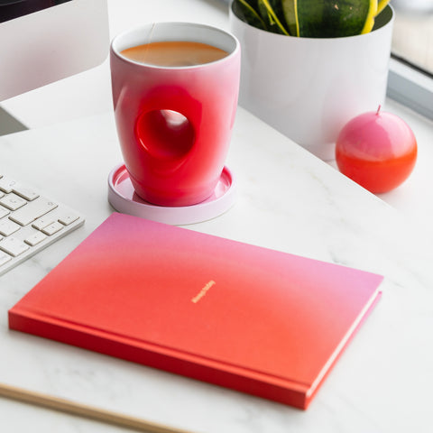 Gradient mug and notebook on a desk with a plant and keyboard in the background