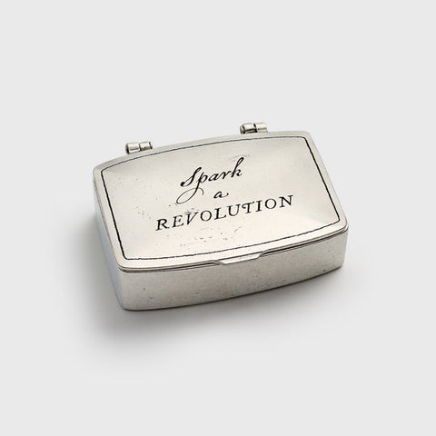 Silver compact with 'Spark a Revolution' text on a white background
