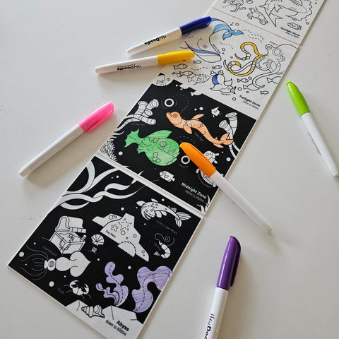 Coloring book with black and white illustrations and markers on a white surface