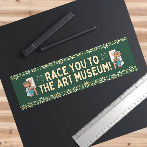 Sticker with 'Race you to the Art Museum!' text on a black surface with pens and a ruler.