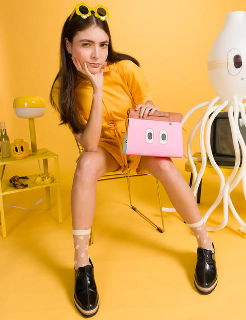 Woman holding a pink box with googly eyes against a yellow background