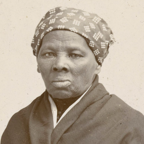 Black and white portrait of a woman wearing a patterned headscarf on a plain background