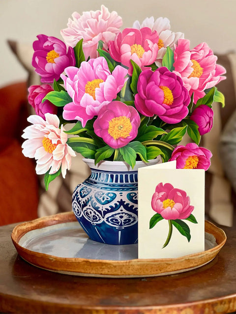 Paper bouquet of pink and purple flowers in a blue and white vase on a wooden tray.