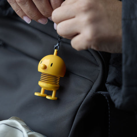 Yellow robot keychain held by a person against a dark background