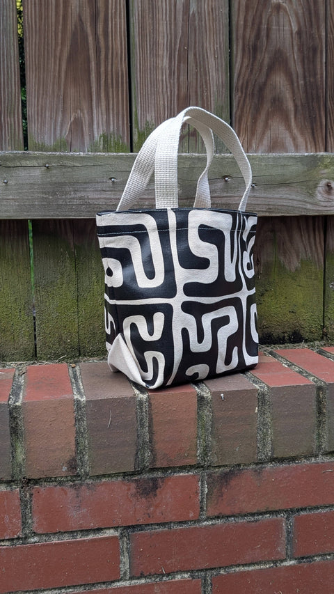Black and white patterned tote bag on a brick ledge with a wooden fence background