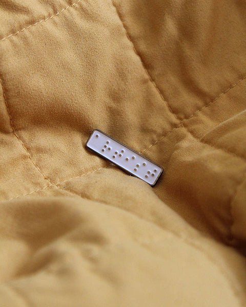 Close-up of a quilted mustard cover with a pin on top.