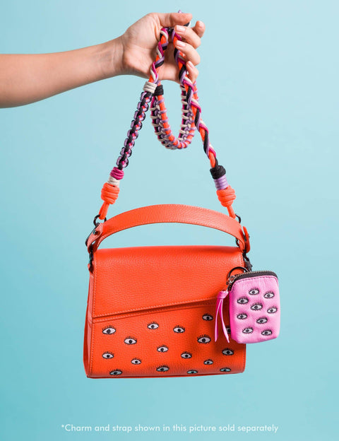 Orange handbag with decorative strap and pink phone case on a light blue background