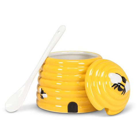 Yellow bee hive-shape jar with with a lid and a white spoon on a white background