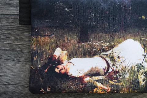 A pouch with a painting of a woman lying in grass on a wooden surface