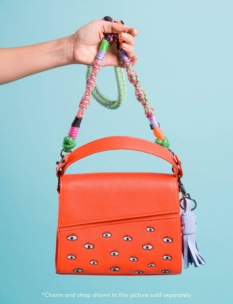 Orange handbag with decorative strap held by a hand against a light blue background