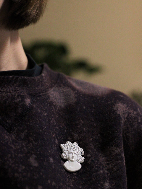 Person wearing a dark purple shirt with a decorative brooch on a blurred background