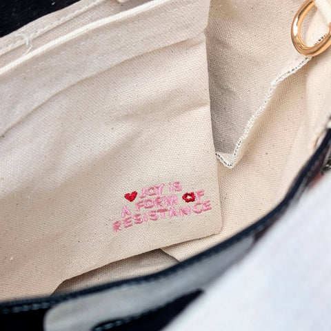 Close-up of a beige fabric bag with embroidered text and heart designs.