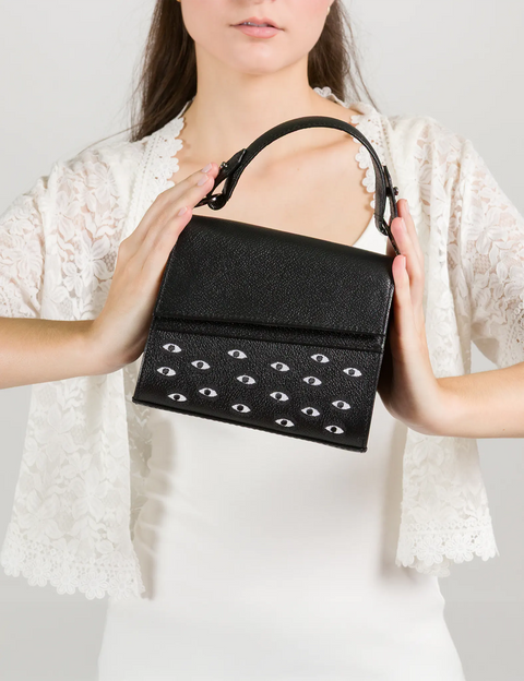 Black handbag with eye-shaped studs held by a person against a white background