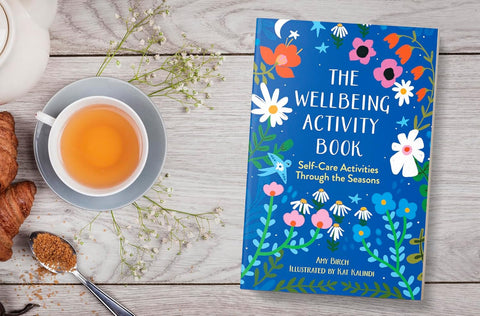 Wellbeing activity book with a cup of tea and croissants on a wooden surface