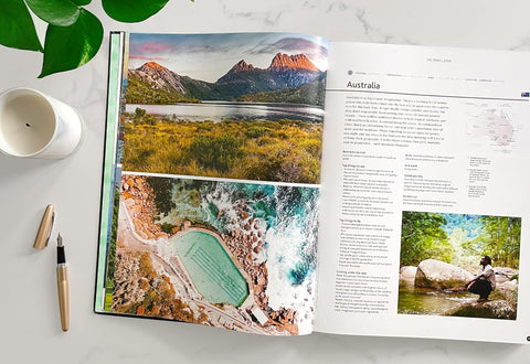 Open book showing scenic images of Australia with a cup and pen on a table.