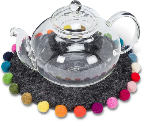 Clear glass teapot on a dark gray felt coaster with colorful pom-poms
