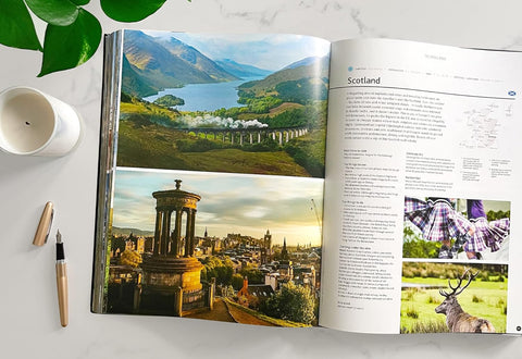 Open book showing scenic images of Scotland with a cup and pen on a table.