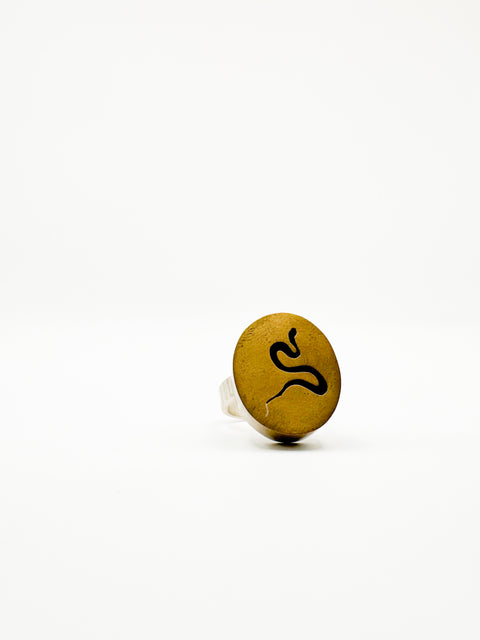 A gold-colored ring with a snake design on it, placed on a white background.