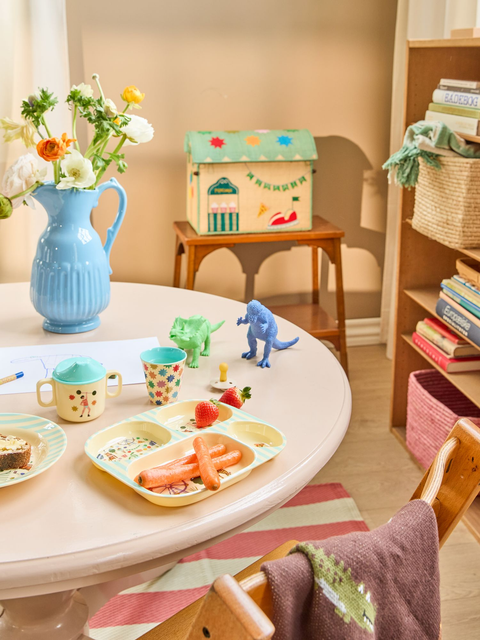 Children's playroom with a table, plates. cups, toys, and books.
