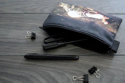 Black pouch with a printed design, pen, and clips on a wooden surface