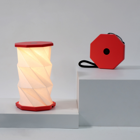 Foldable lamp with red base and white shade on a gray surface