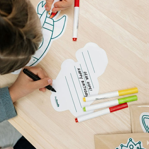 Child coloring a birthday card with markers on a wooden table