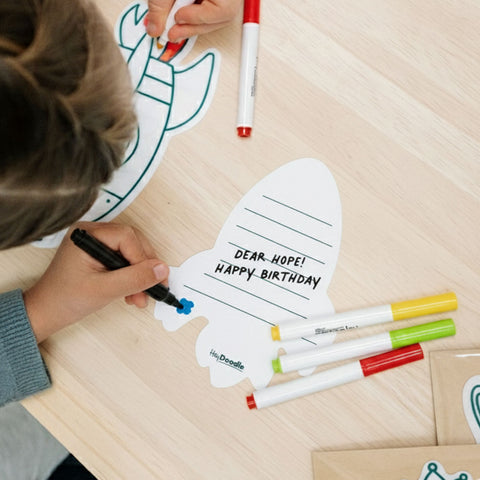 Child coloring a birthday card with markers on a wooden table