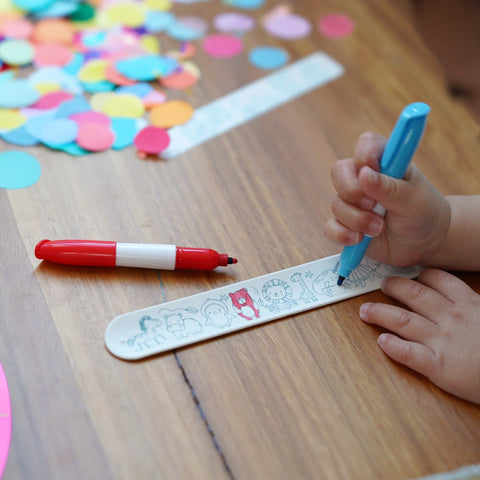 Child coloring on a craft bracelet with markers on a wooden table
