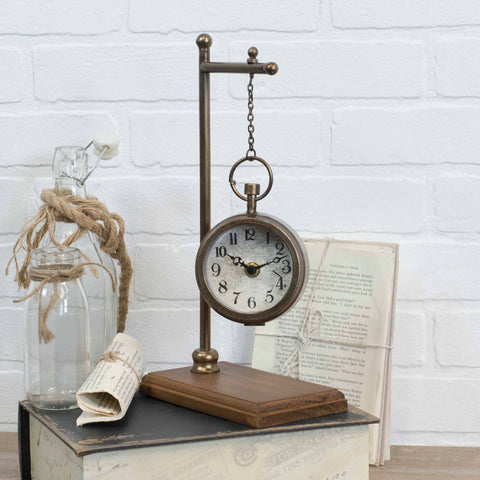 Decorative clock on a stand with a jar and book against a white brick wall.
