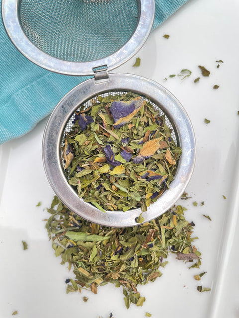 Tea infuser with dried herbs on a white surface